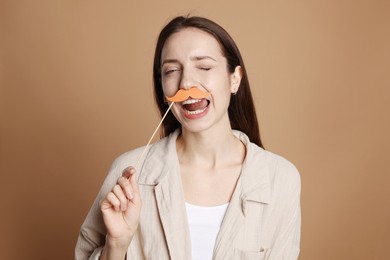 Funny woman with fake paper mustache on brown background