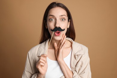 Surprised woman with fake paper mustache on brown background