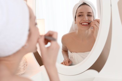 Happy woman plucking her mustache with tweezers near mirror at home