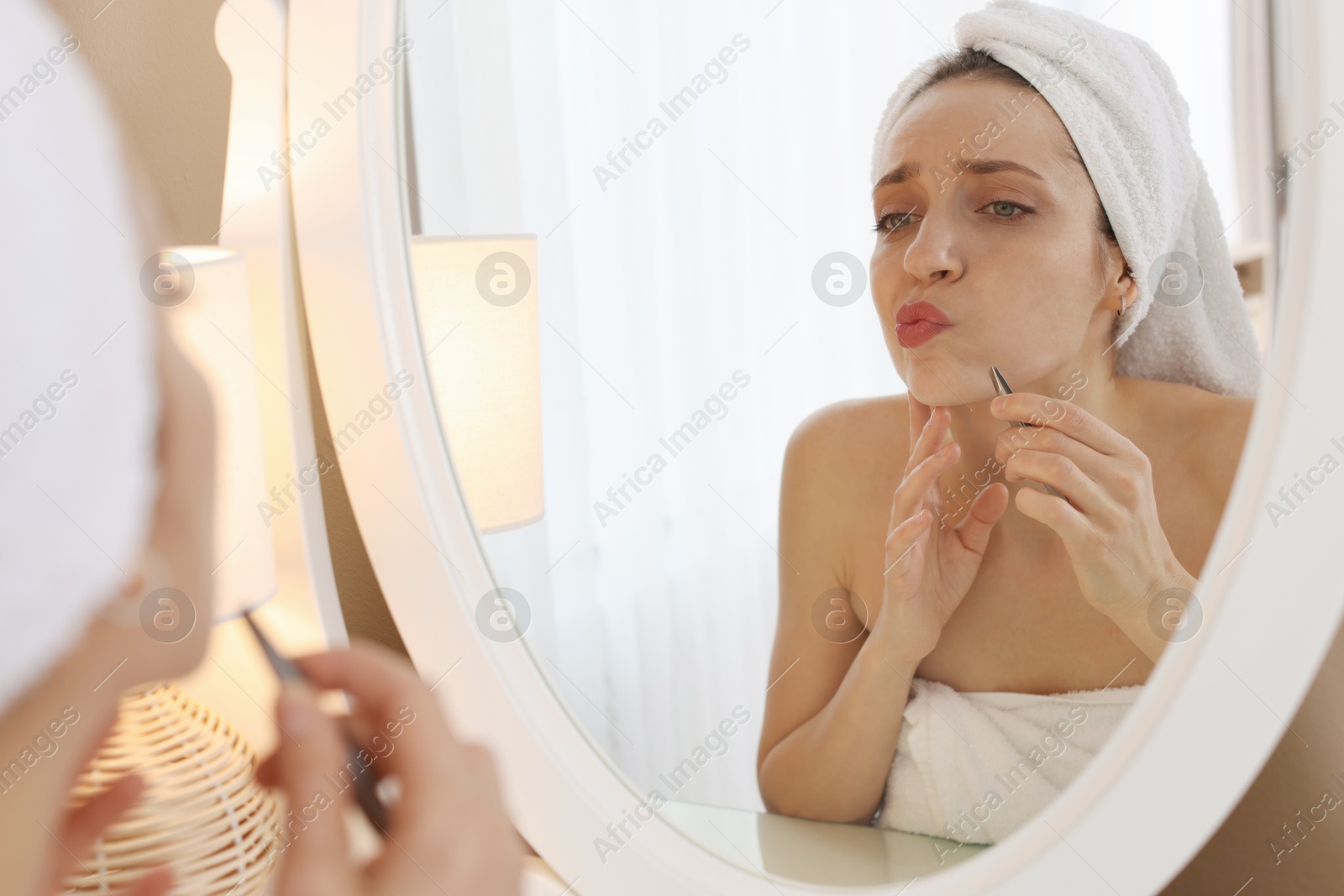 Photo of Beautiful woman plucking her mustache with tweezers near mirror at home