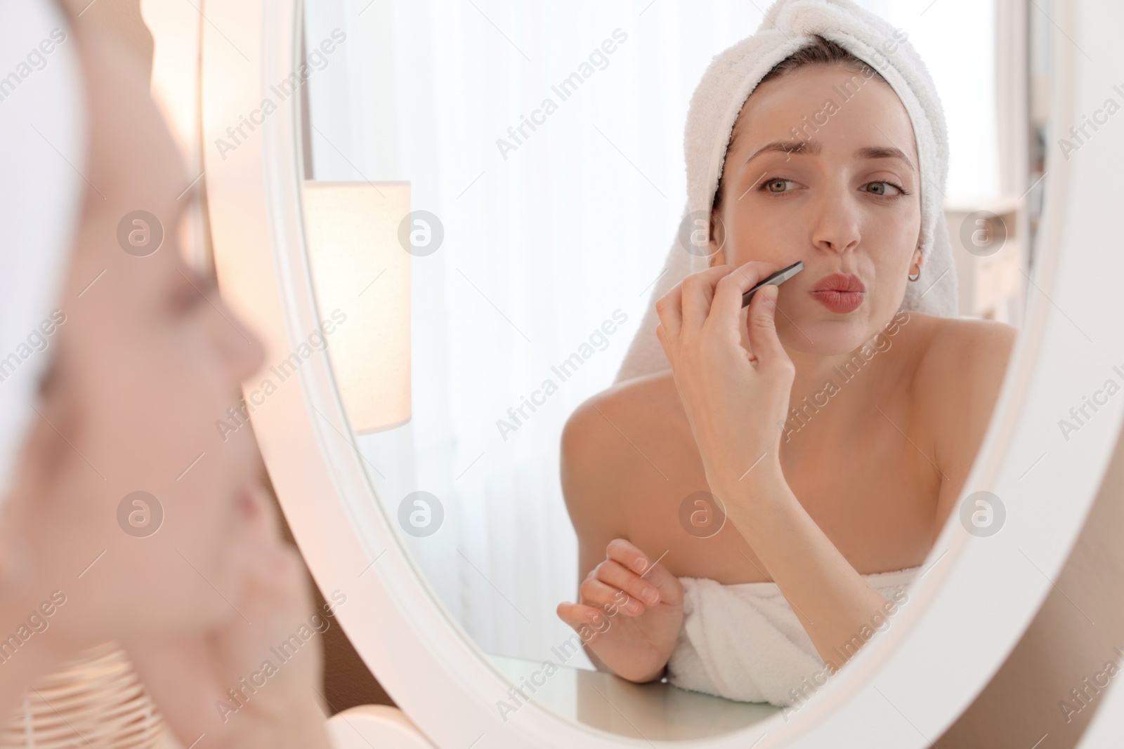 Photo of Beautiful woman plucking her mustache with tweezers near mirror at home