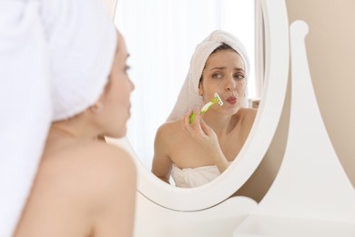 Photo of Beautiful woman shaving her mustache with razor near mirror at home