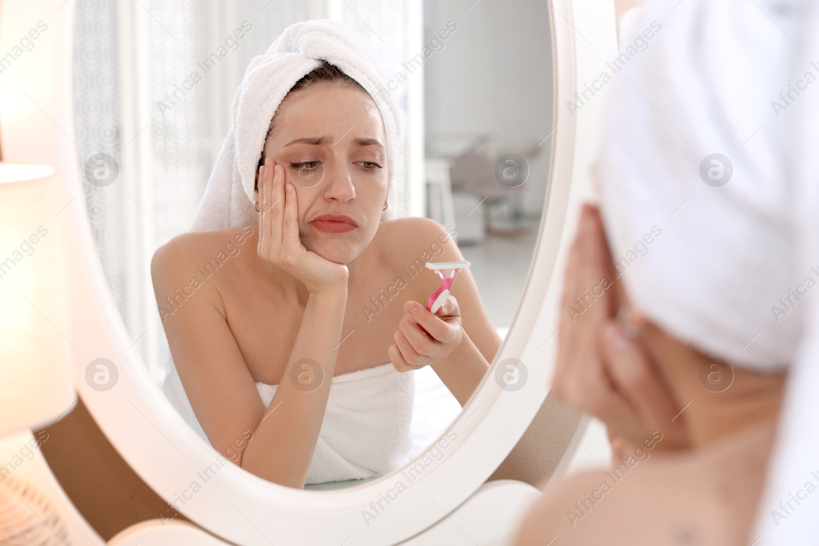 Photo of Disappointed woman with razor near mirror at home. Hair removal tool