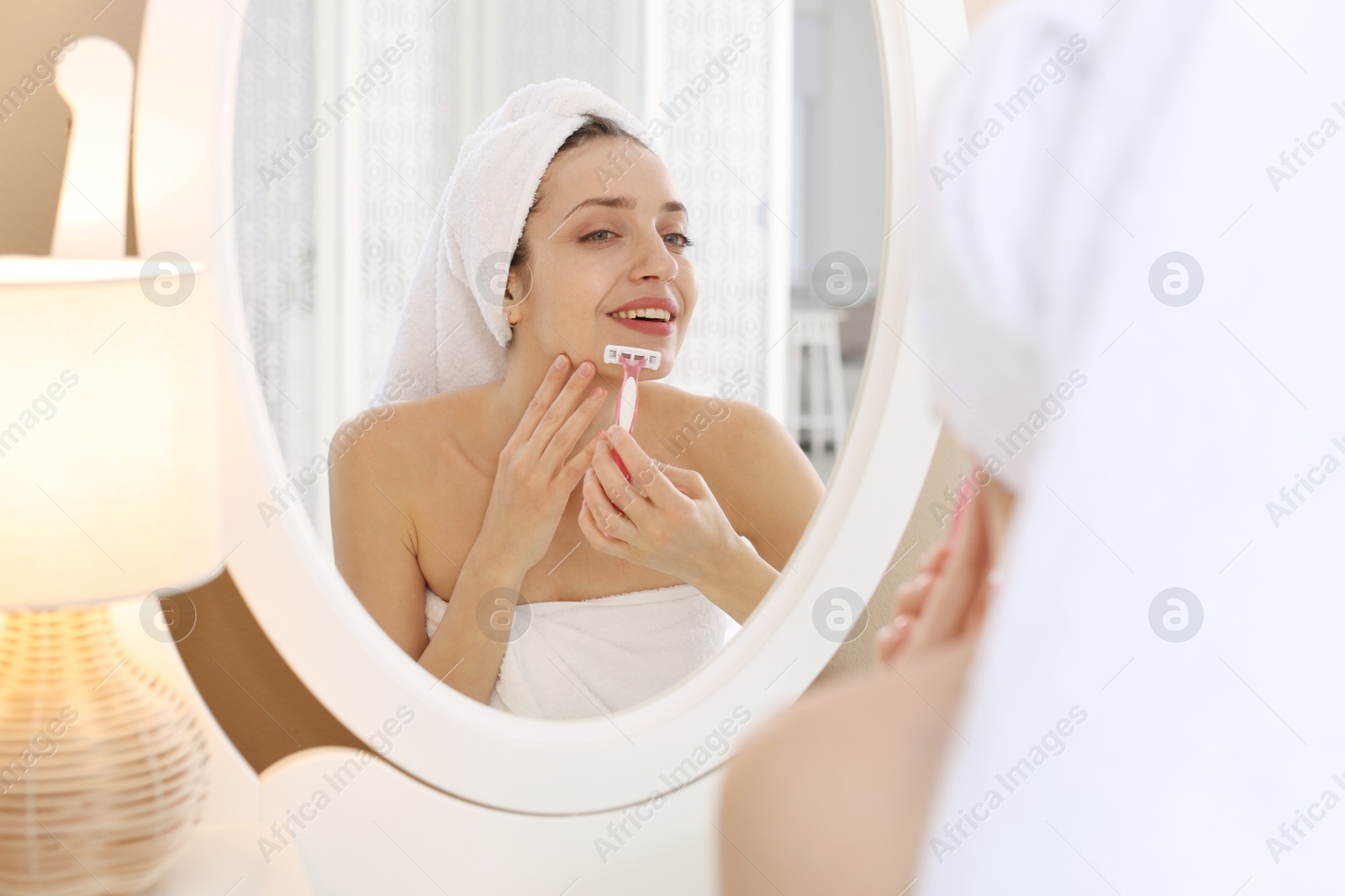 Photo of Happy woman shaving her mustache with razor near mirror at home