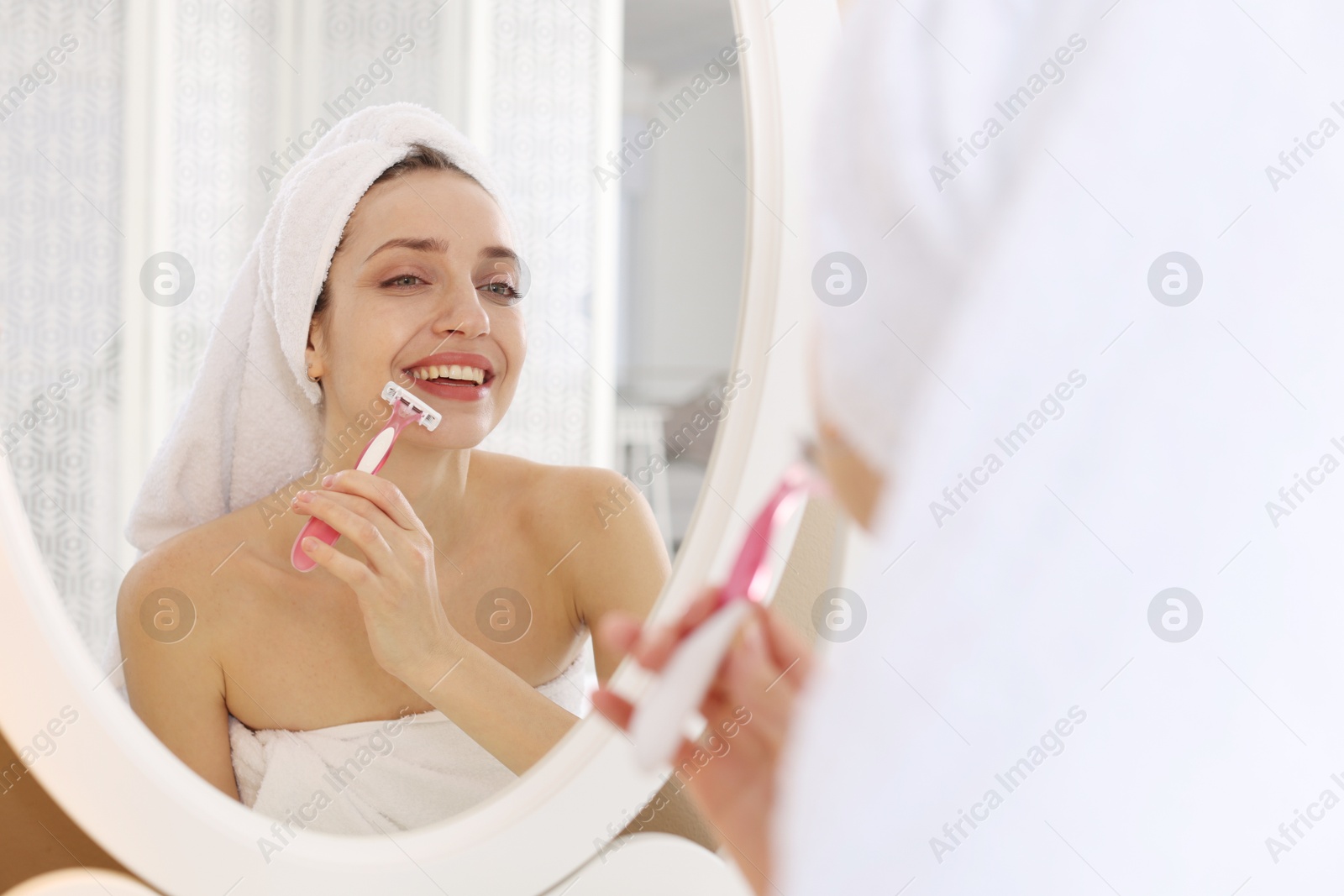 Photo of Happy woman shaving her mustache with razor near mirror at home