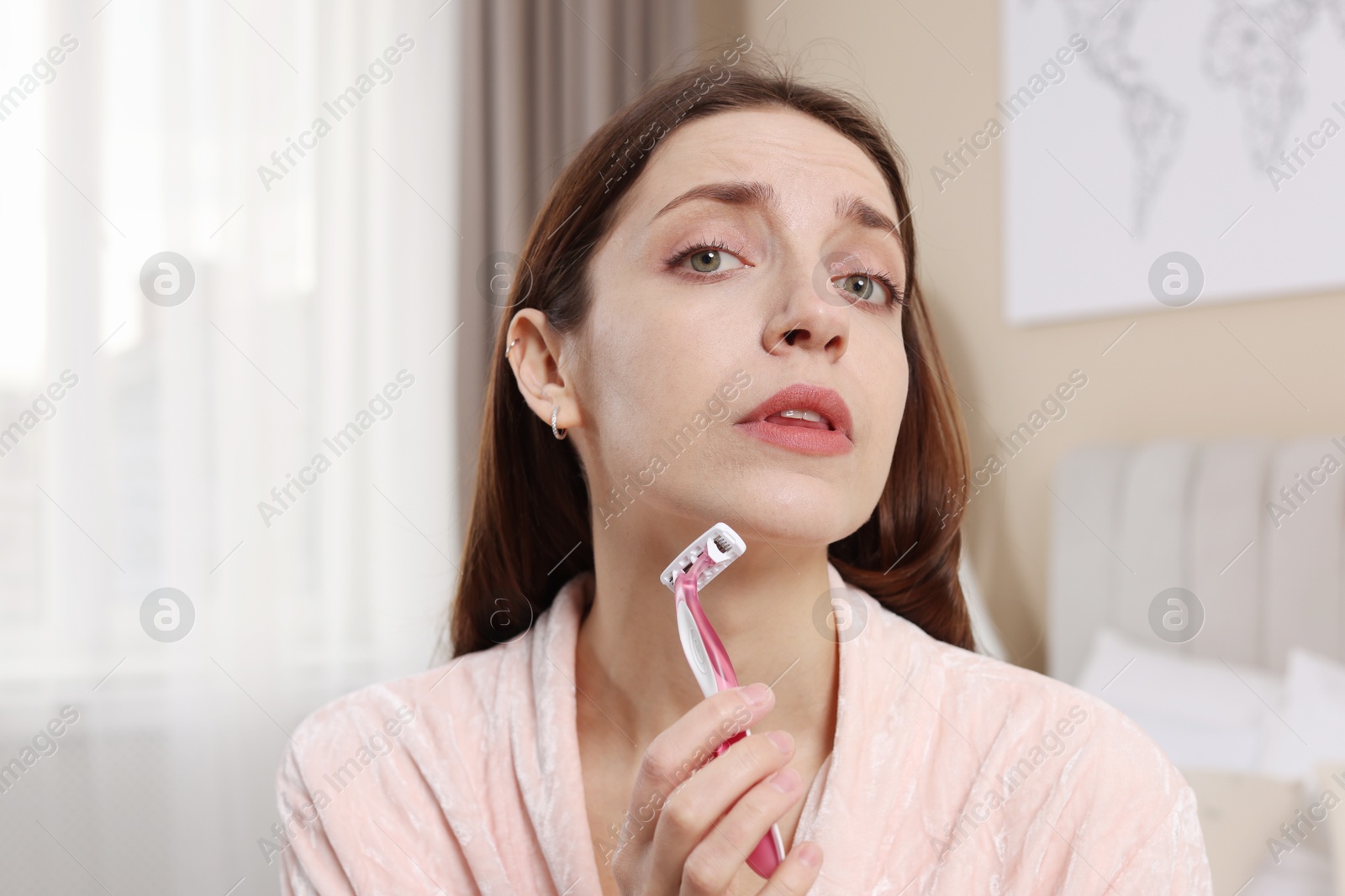 Photo of Beautiful woman shaving her facial hair with razor at home