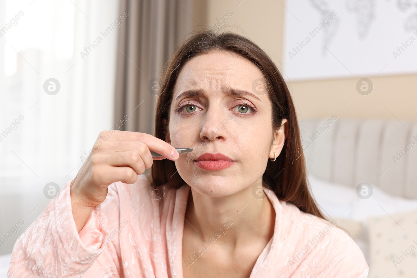 Photo of Beautiful woman plucking her mustache with tweezers at home