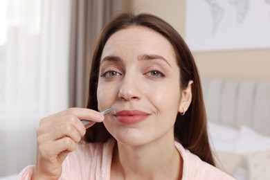 Beautiful woman plucking her mustache with tweezers at home