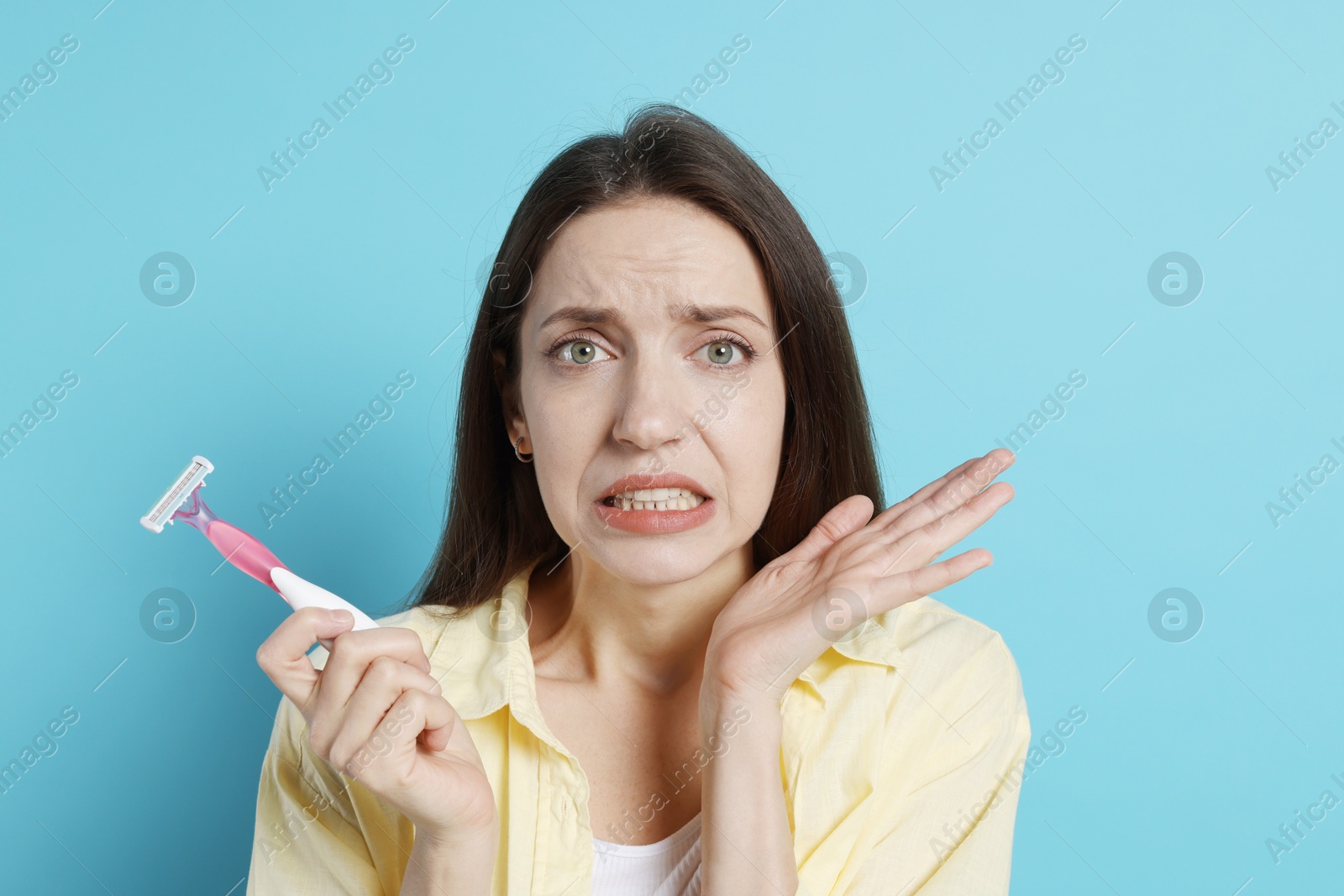 Photo of Emotional woman with razor on light blue background. Hair removal tool