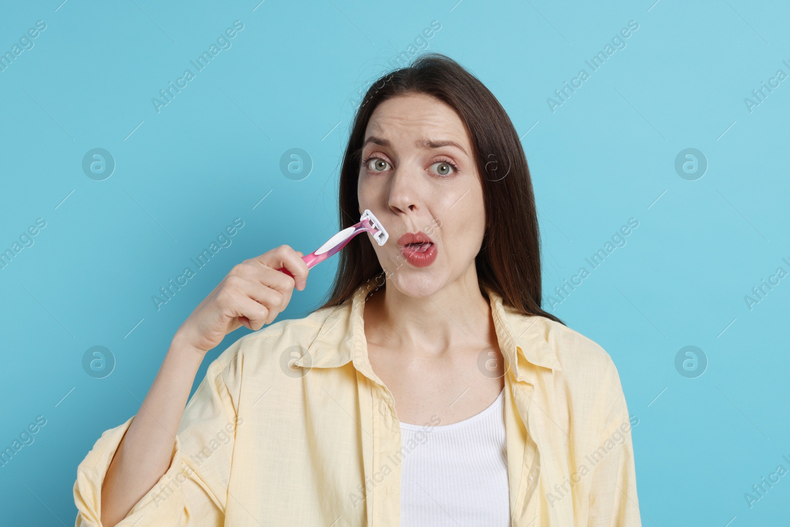 Photo of Woman shaving her mustache with razor on light blue background