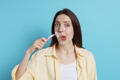 Woman shaving her mustache with razor on light blue background