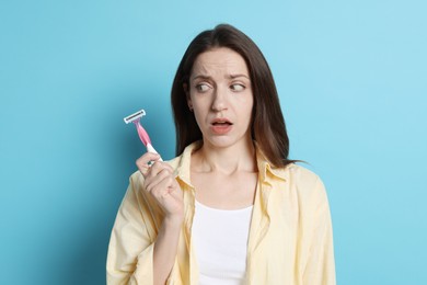 Photo of Emotional woman with razor on light blue background. Hair removal tool