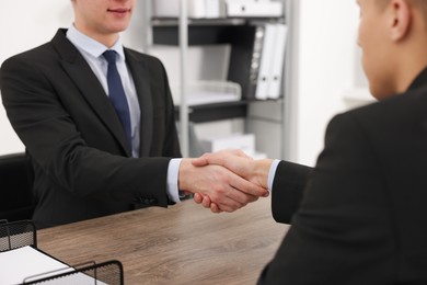 Photo of Businessmen shaking hands at wooden desk in office, closeup