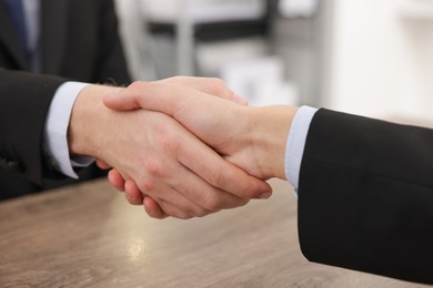 Photo of Businessmen shaking hands at wooden desk in office, closeup