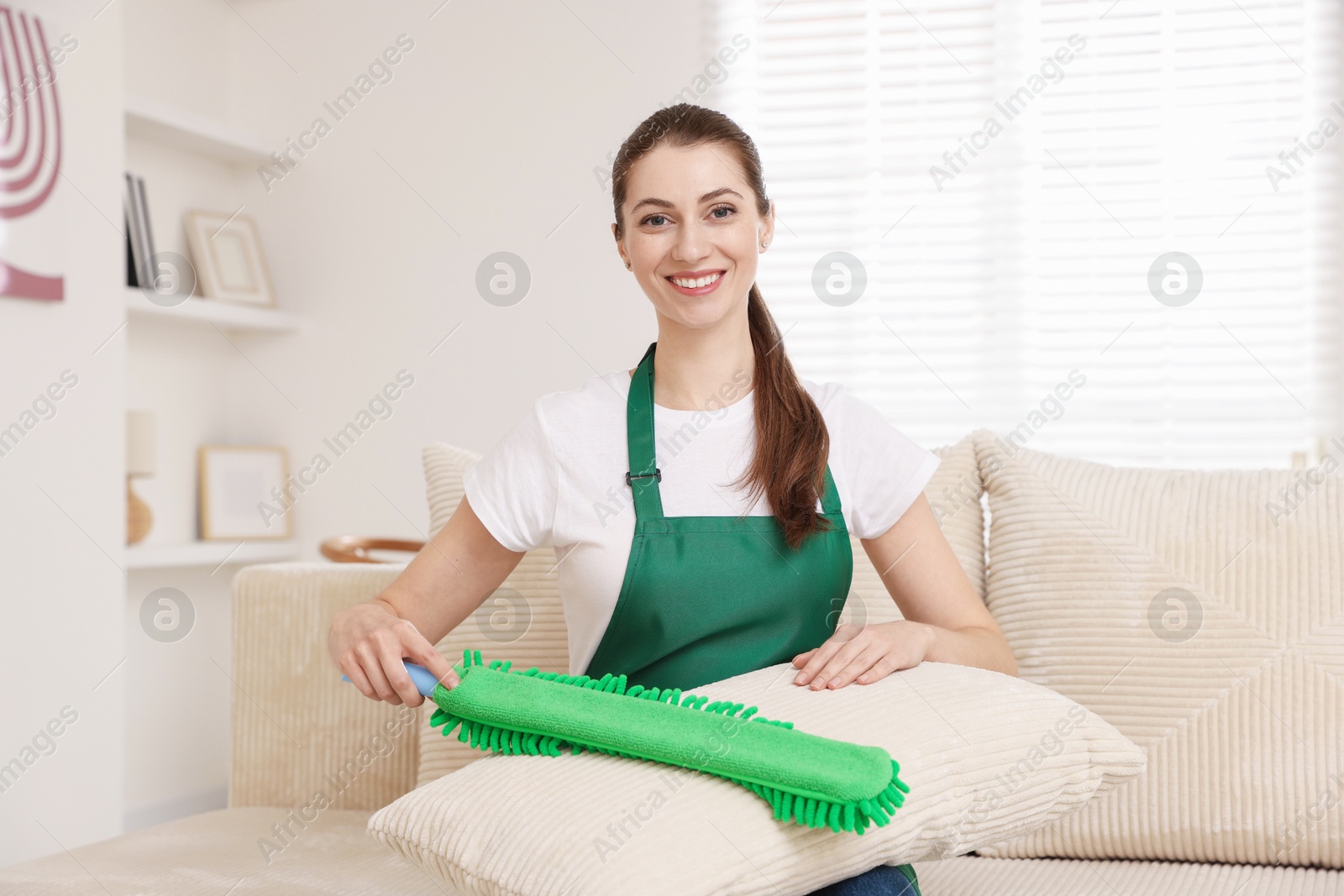 Photo of Janitor cleaning sofa cushion with duster at home