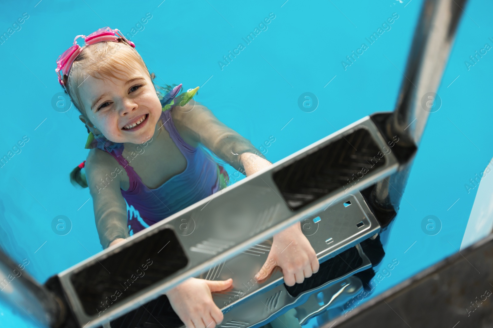 Photo of Little girl with goggles getting out of swimming pool, above view