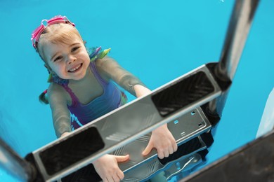 Little girl with goggles getting out of swimming pool, above view