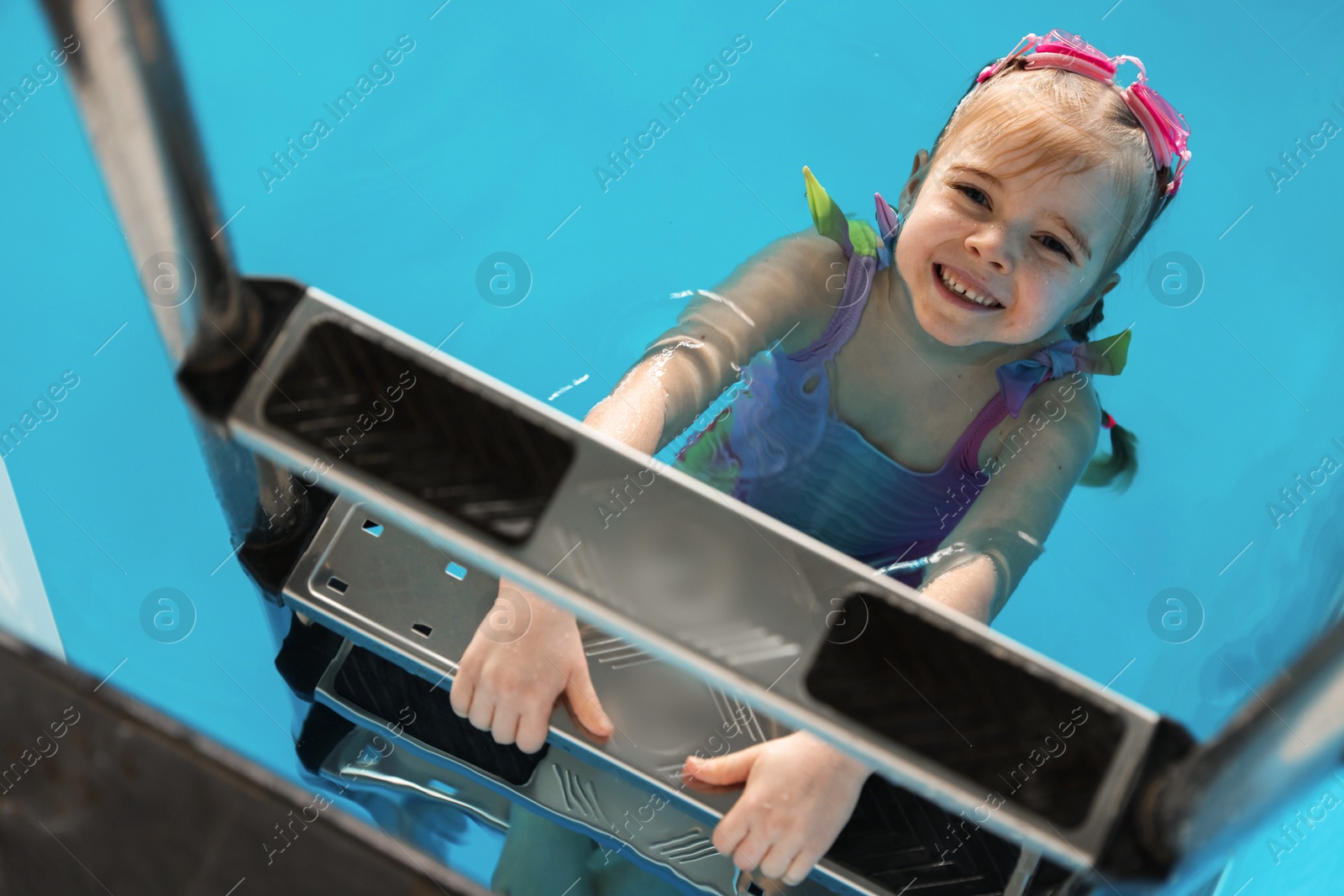 Photo of Little girl with goggles getting out of swimming pool, above view