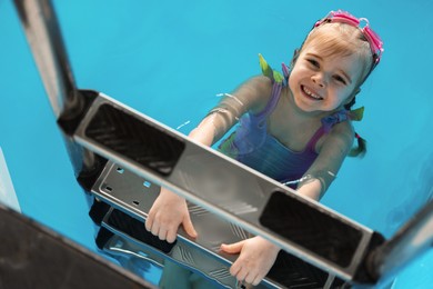 Photo of Little girl with goggles getting out of swimming pool, above view