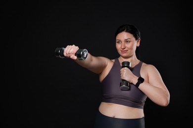 Plus size woman in gym clothes doing exercise with dumbbells on black background, space for text