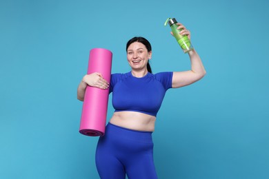 Plus size woman in gym clothes with water bottle and mat on light blue background