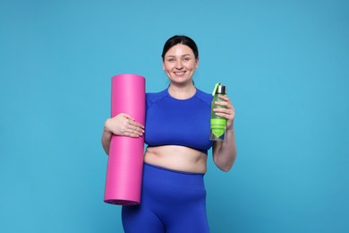 Plus size woman in gym clothes with water bottle and mat on light blue background