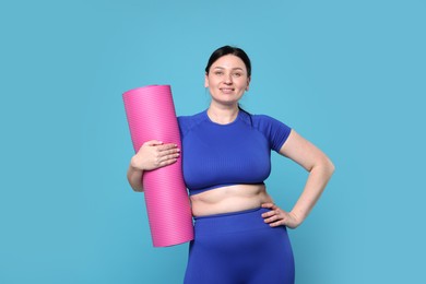 Photo of Plus size woman in gym clothes with fitness mat on light blue background