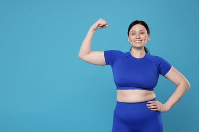 Plus size woman in gym clothes showing her bicep on light blue background, space for text