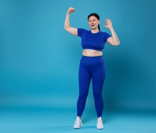 Plus size woman in gym clothes showing ok gesture on light blue background, space for text