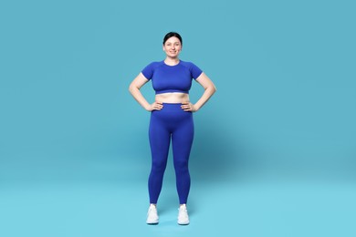 Plus size woman in gym clothes on light blue background