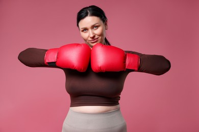 Photo of Plus size woman in gym clothes with boxing gloves on pink background