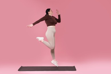 Photo of Plus size woman in gym clothes exercising on pink background