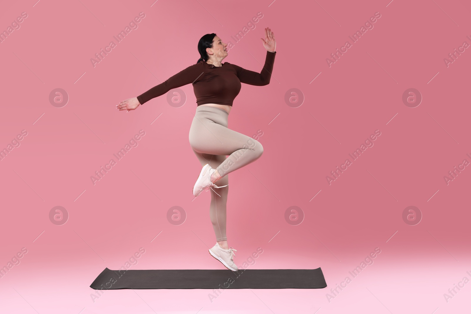 Photo of Plus size woman in gym clothes exercising on pink background