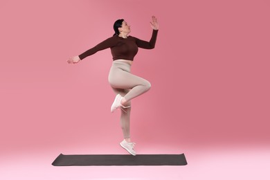 Plus size woman in gym clothes exercising on pink background