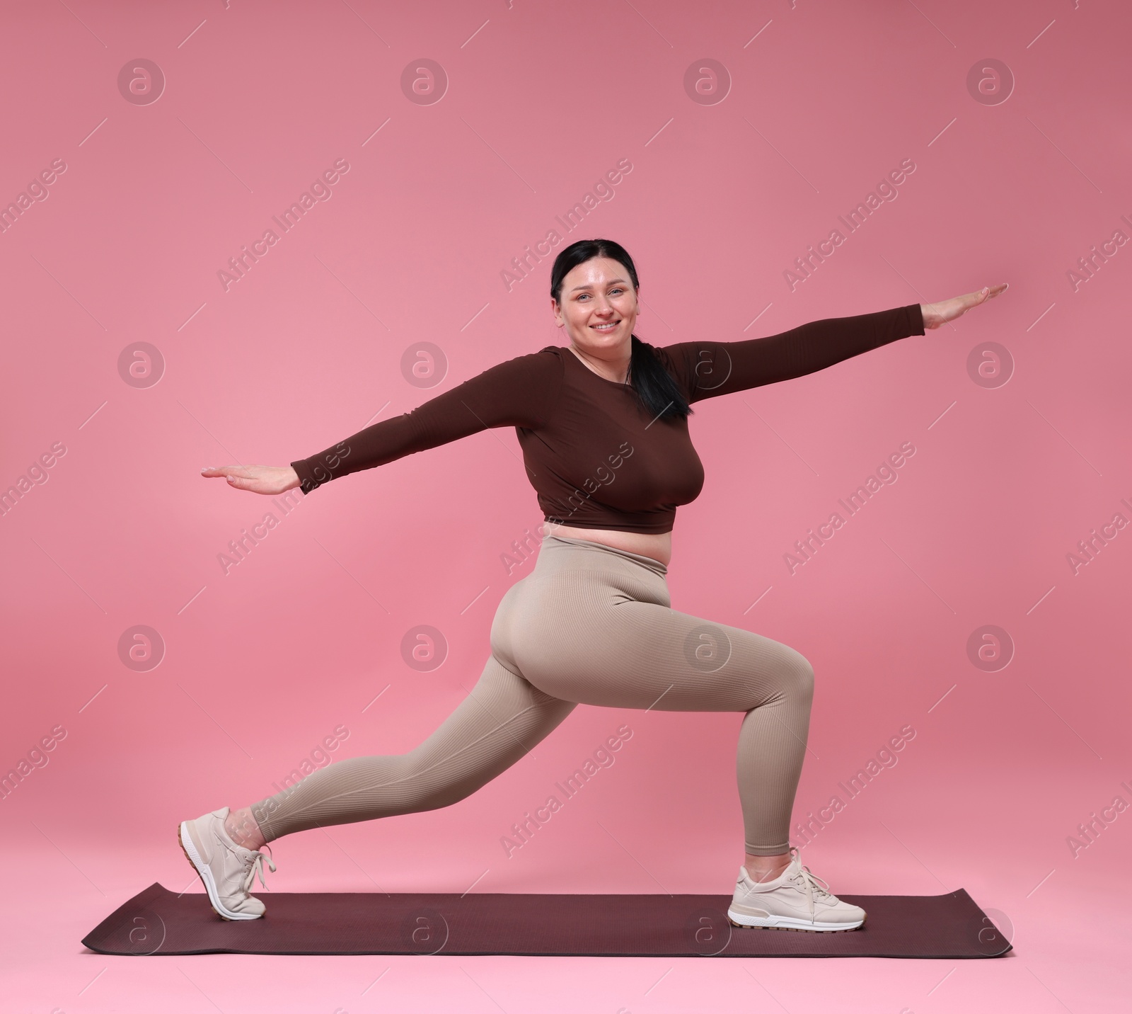 Photo of Plus size woman in gym clothes exercising on pink background