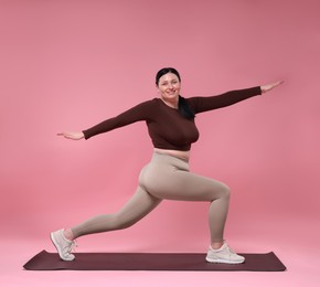 Photo of Plus size woman in gym clothes exercising on pink background