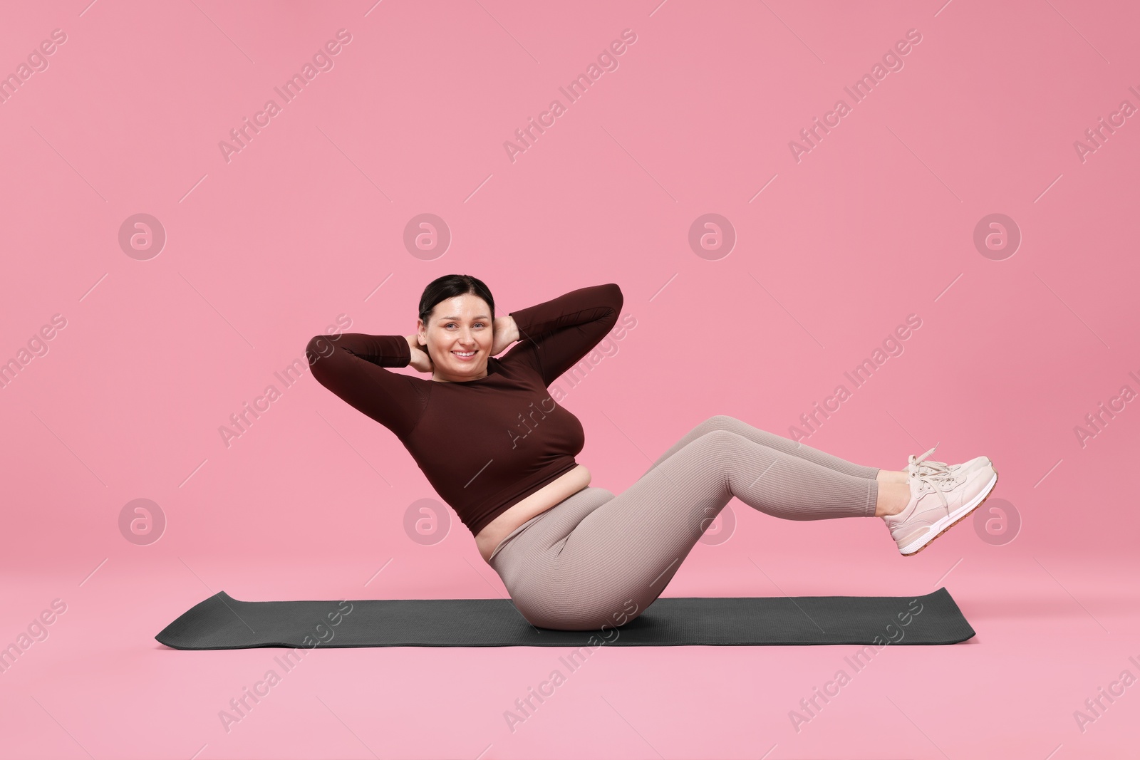 Photo of Plus size woman in gym clothes exercising on pink background