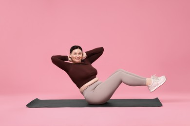 Plus size woman in gym clothes exercising on pink background