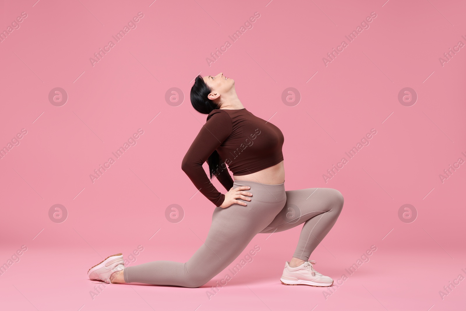 Photo of Plus size woman in gym clothes exercising on pink background