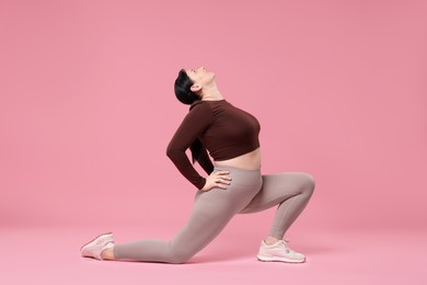 Plus size woman in gym clothes exercising on pink background