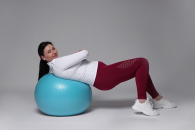 Plus size woman in gym clothes with fitness ball on grey background