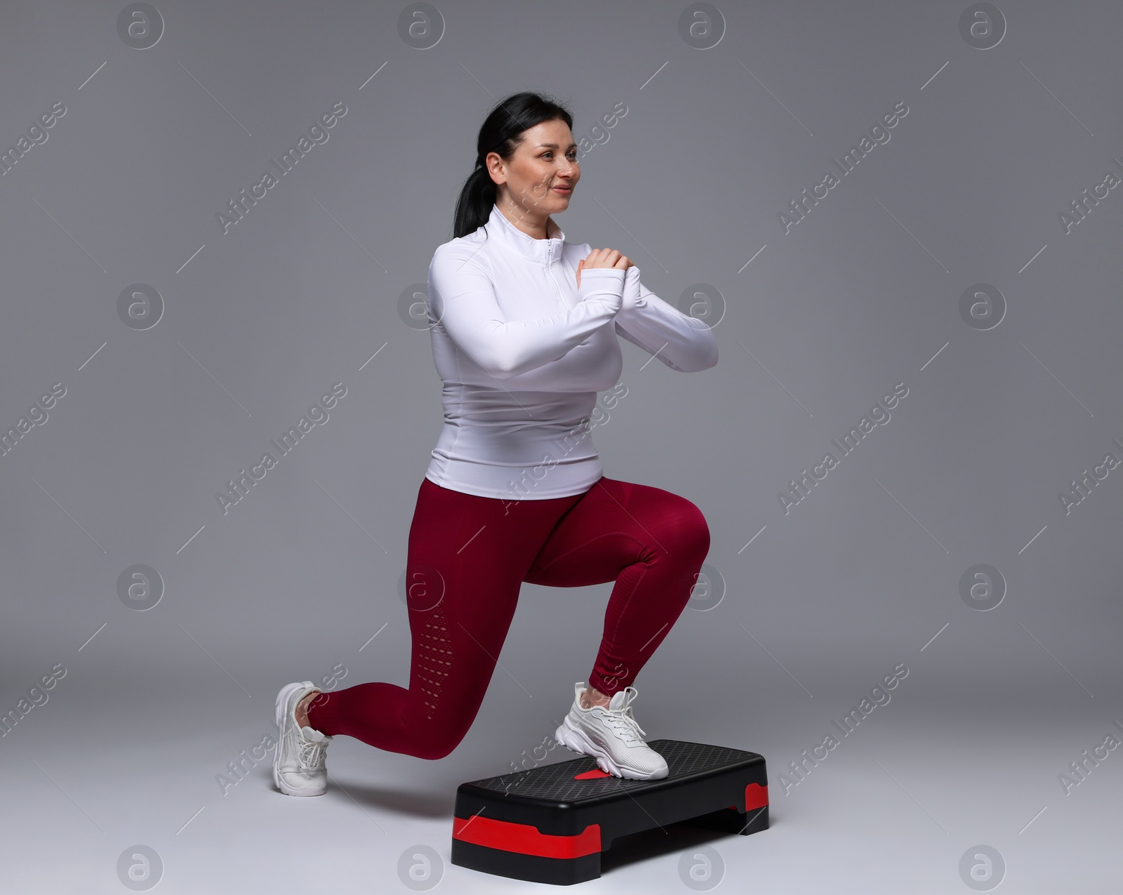 Photo of Plus size woman in gym clothes doing exercise with step platform on grey background