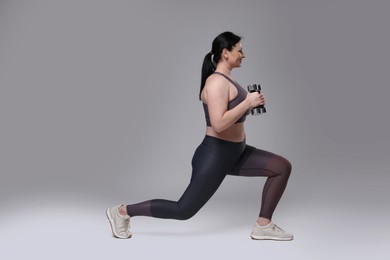 Plus size woman in gym clothes doing exercise with dumbbells on grey background