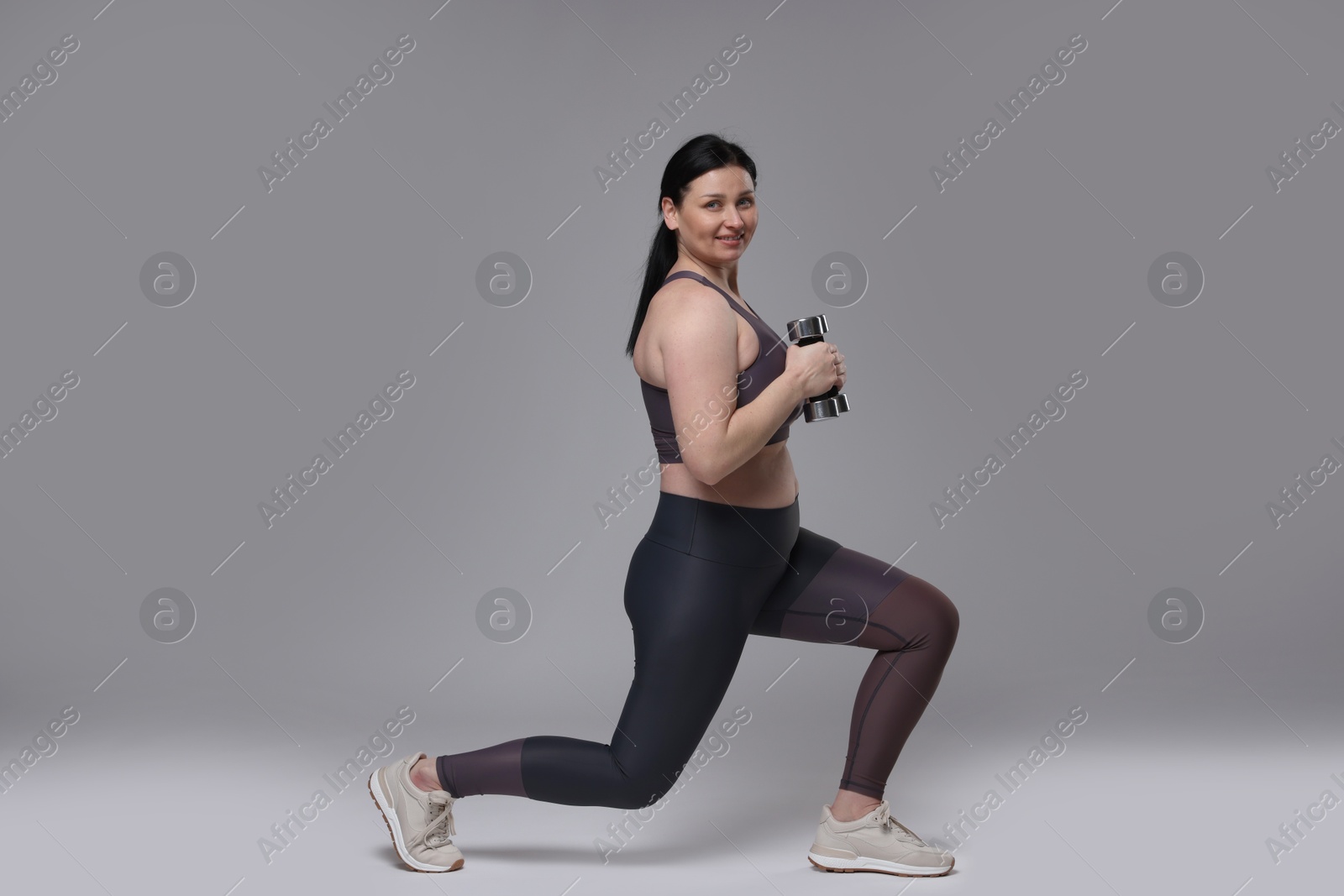 Photo of Plus size woman in gym clothes doing exercise with dumbbells on grey background