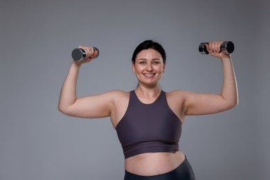 Plus size woman in gym clothes doing exercise with dumbbells on grey background