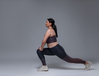 Plus size woman in gym clothes doing exercising on grey background