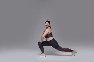 Plus size woman in gym clothes doing exercising on grey background