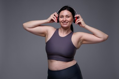 Photo of Plus size woman in gym clothes and headphones on grey background