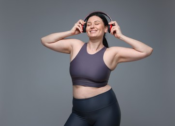 Plus size woman in gym clothes and headphones on grey background