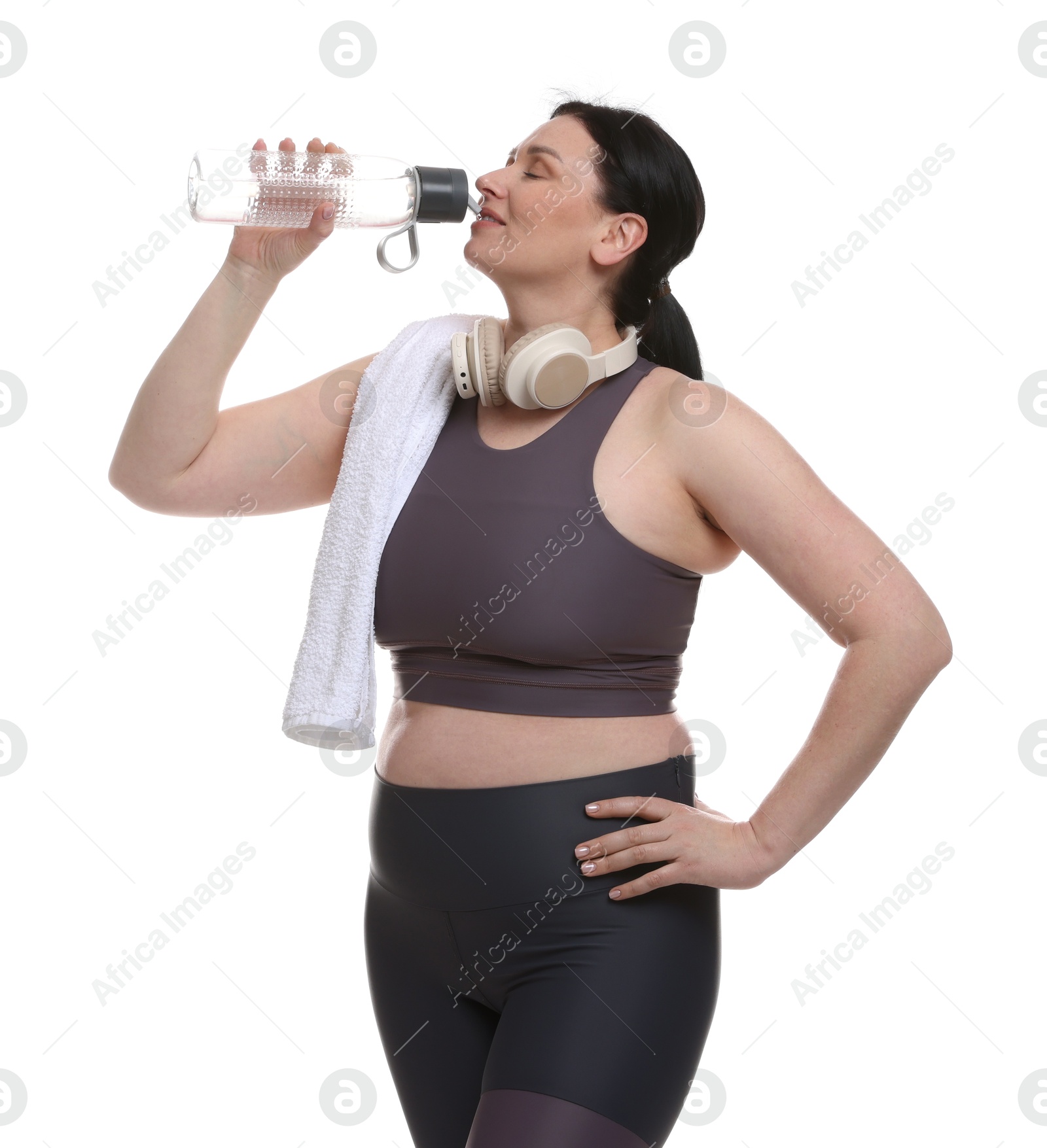 Photo of Plus size woman in gym clothes with water bottle, headphones and towel on white background